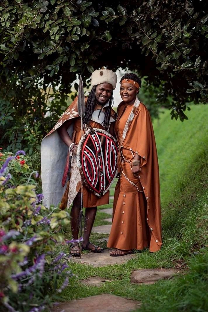 two men dressed in african clothing standing next to each other on a path surrounded by flowers