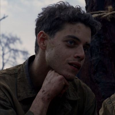 a young man with freckles on his face sitting next to a tree