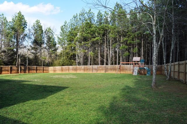 an empty backyard with grass and trees in the back ground, surrounded by wooden fences