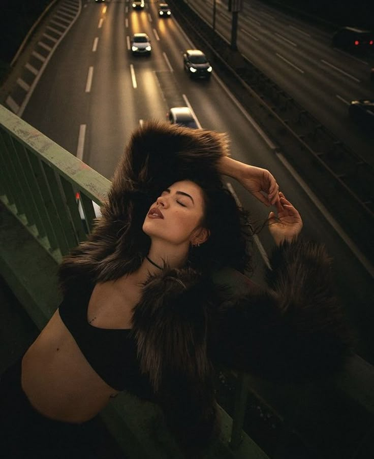 a woman wearing a fur coat on top of a balcony next to a street at night