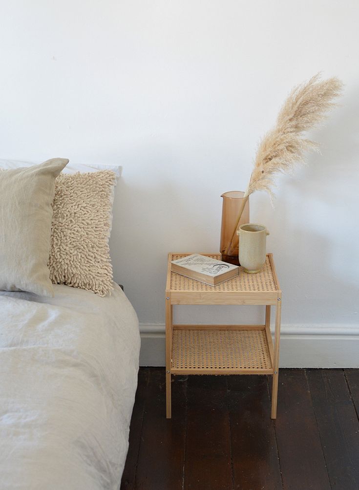 a small table with a plant on top of it next to a bed and pillows