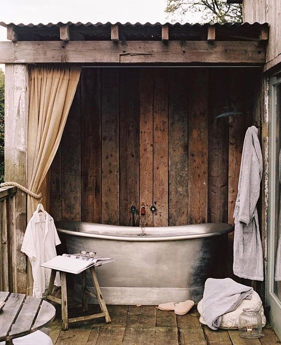 an outdoor bathtub on a wooden deck next to a window with curtains and towels