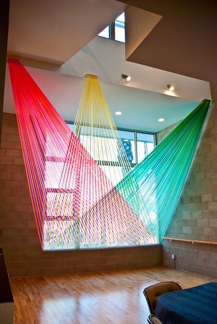 a room with a large window and colorful hammock hanging from it's ceiling