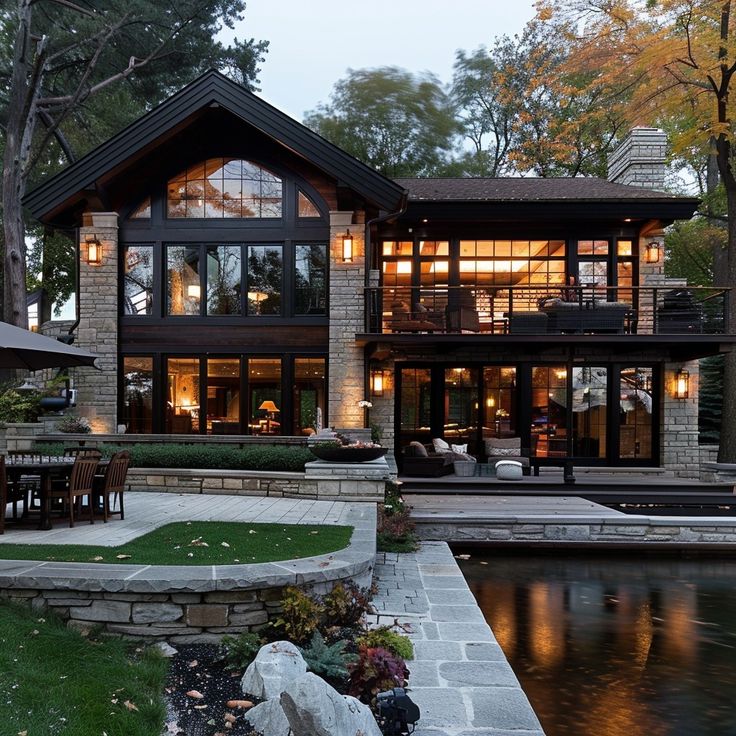 a large house sitting on top of a lush green field next to a lake in front of a forest