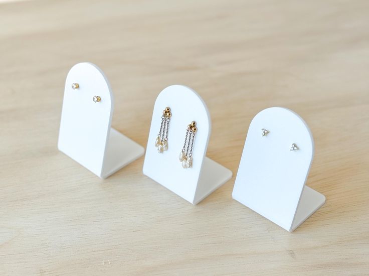 three small white jewelry stands on a wooden table with two pairs of earrings hanging from them