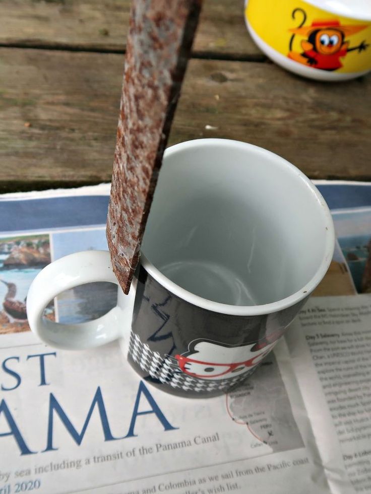 a coffee cup sitting on top of a wooden table next to a newspaper with a stick sticking out of it