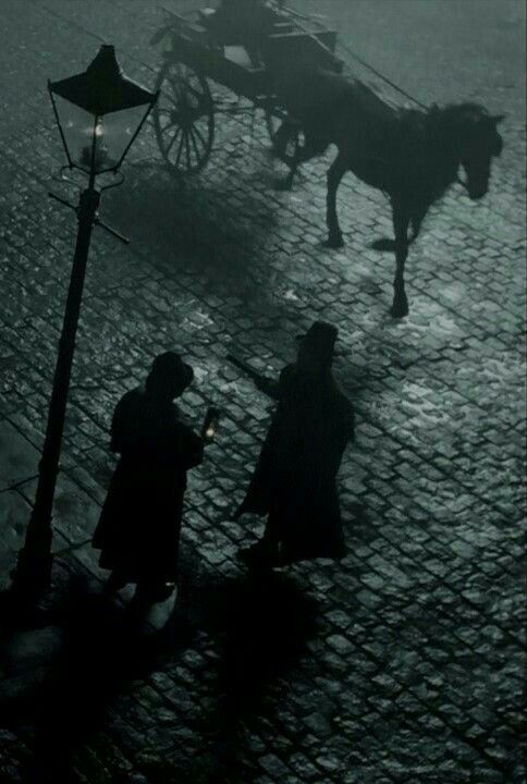 two people standing next to a horse drawn carriage on a cobblestone street in the rain