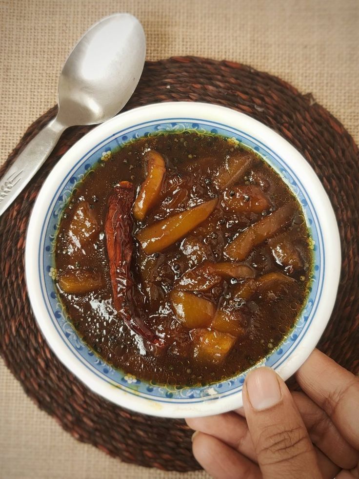 a person holding a bowl of food on top of a woven place mat with spoon