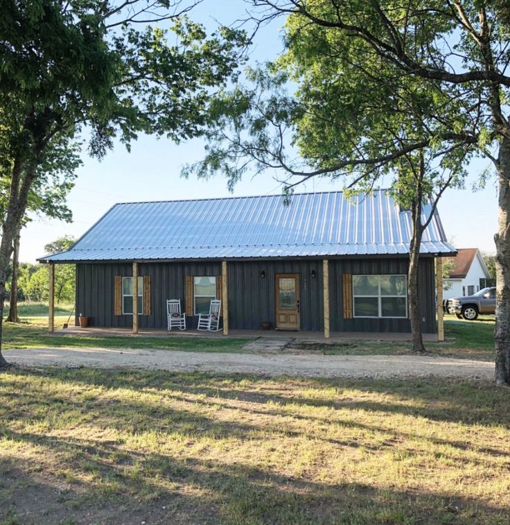 a small house with a metal roof in the middle of a field next to trees