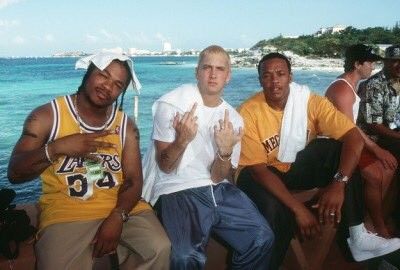 four young men sitting on the edge of a pier next to the ocean, one holding his hand up