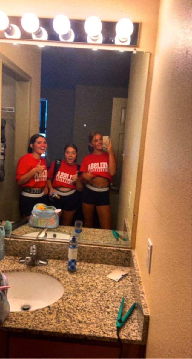 three women in red shirts standing in front of a bathroom mirror