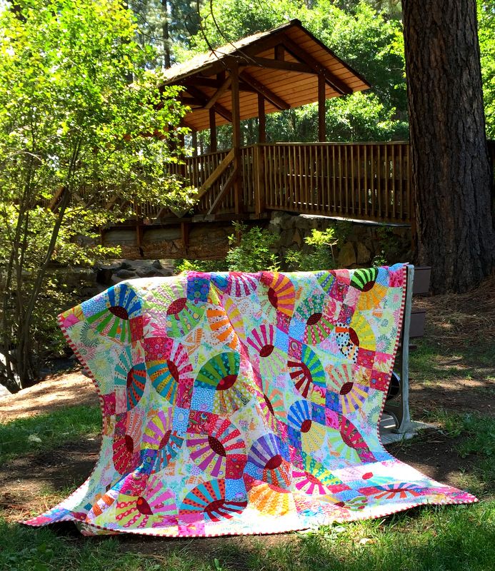 a colorful quilt sitting on the ground next to a tree