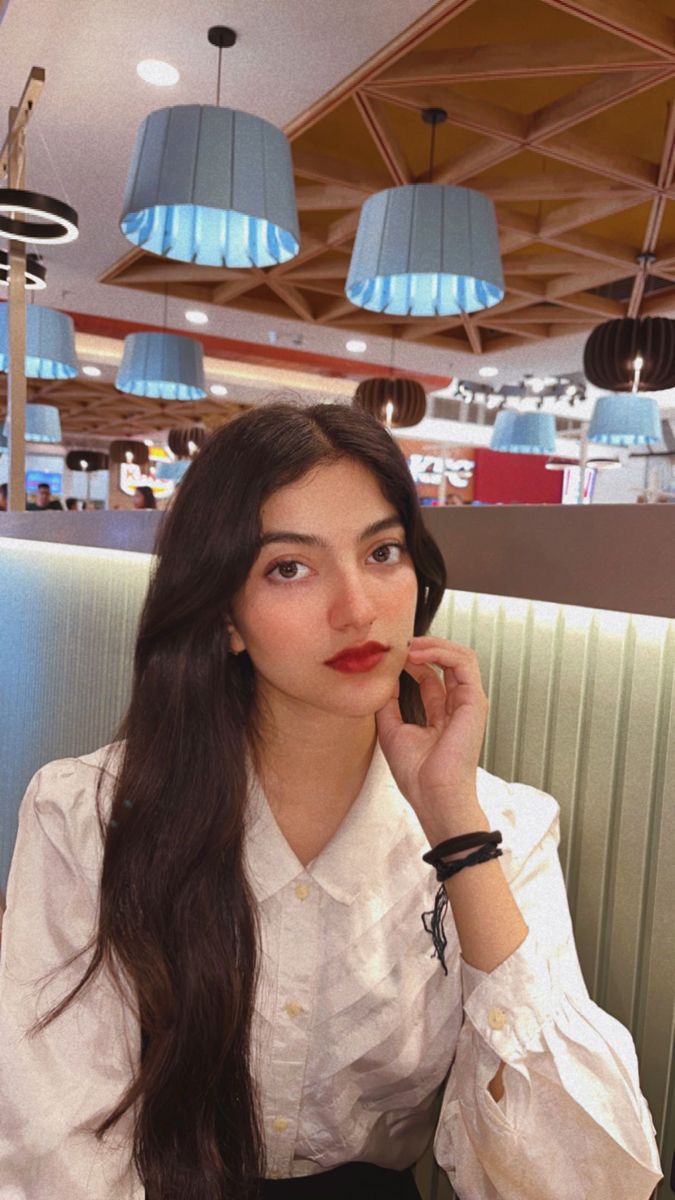 a woman sitting at a table with a cell phone to her ear and wearing a white shirt