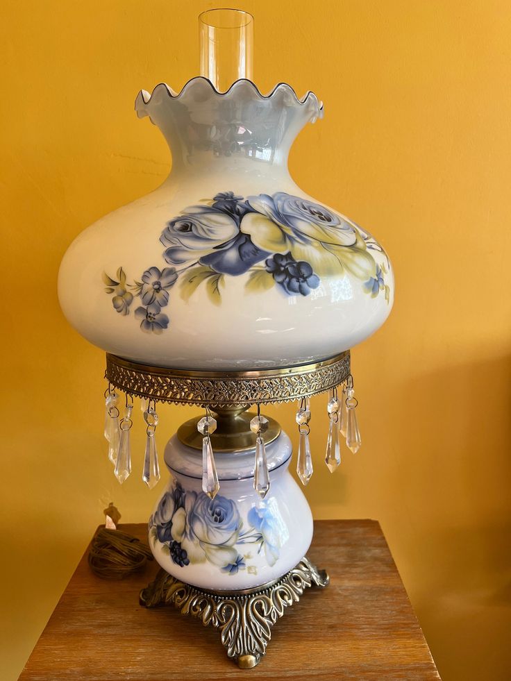 a white vase sitting on top of a wooden table next to a lamp shade with flowers painted on it