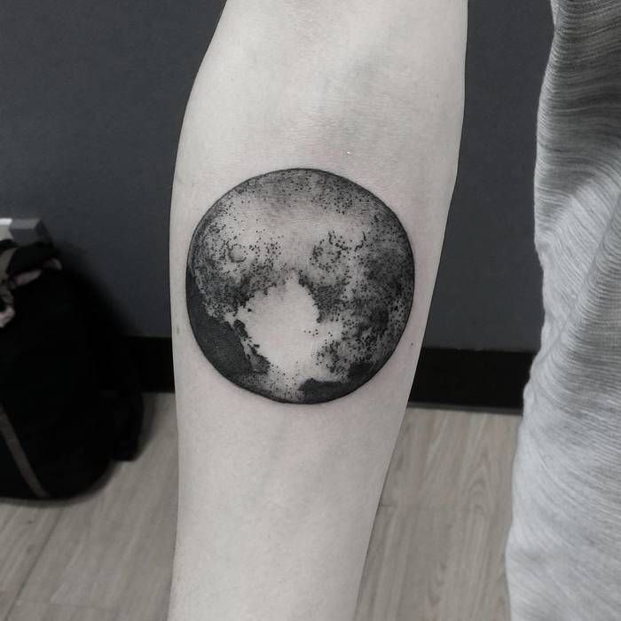 a black and white photo of a half moon tattoo on the right forearm, with an ink spot in the middle