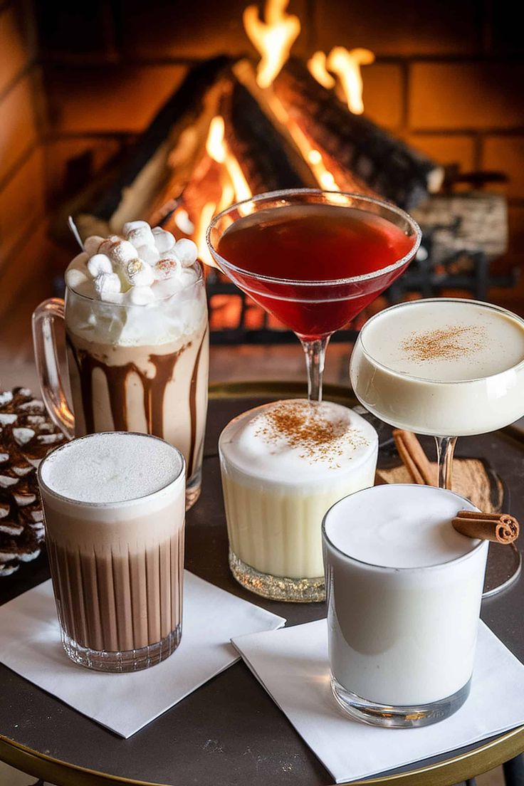 four different drinks are sitting on a table near a fire place and napkins that have been placed around them