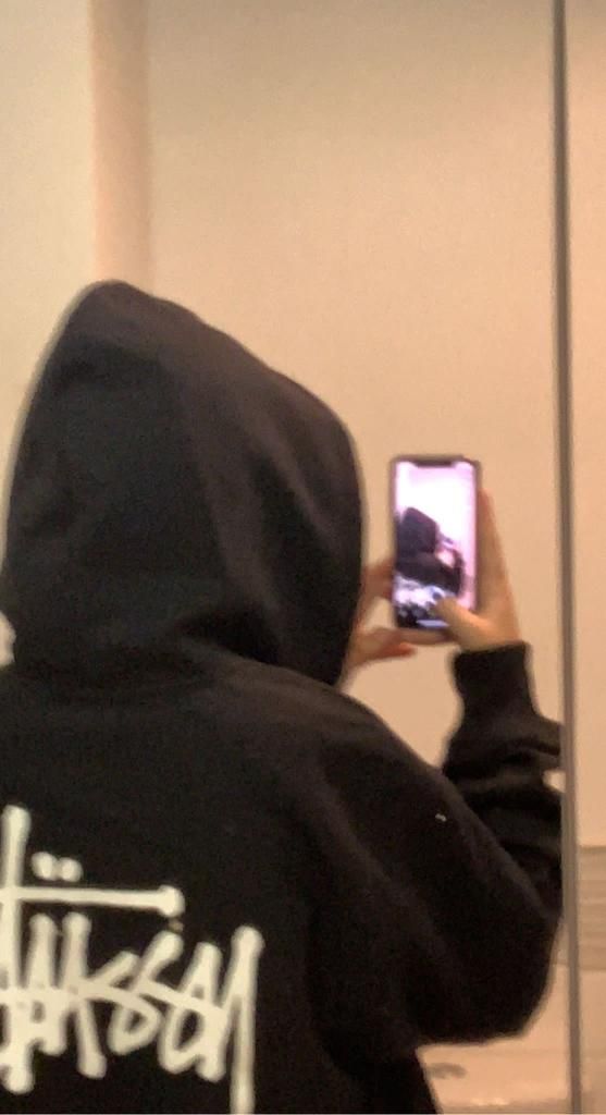 a person in a black hoodie taking a selfie with their cell phone while standing next to a mirror