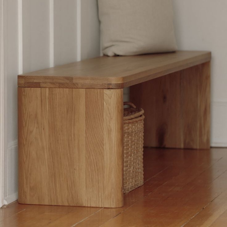 a wooden bench with a basket under it on the floor next to a white wall