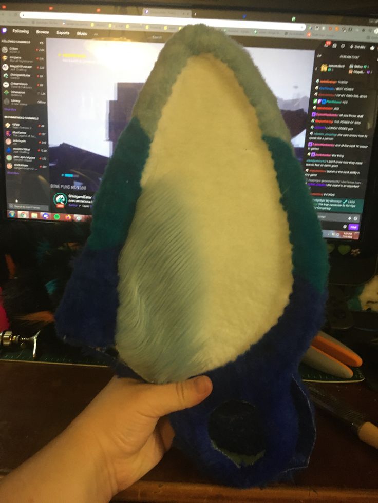 a hand is holding a stuffed animal in front of a computer screen and desk top