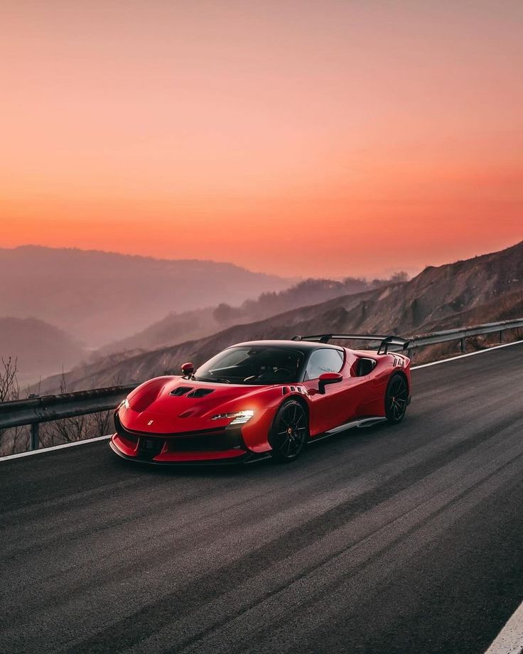 a red sports car is driving down the road at sunset or dawn with mountains in the background