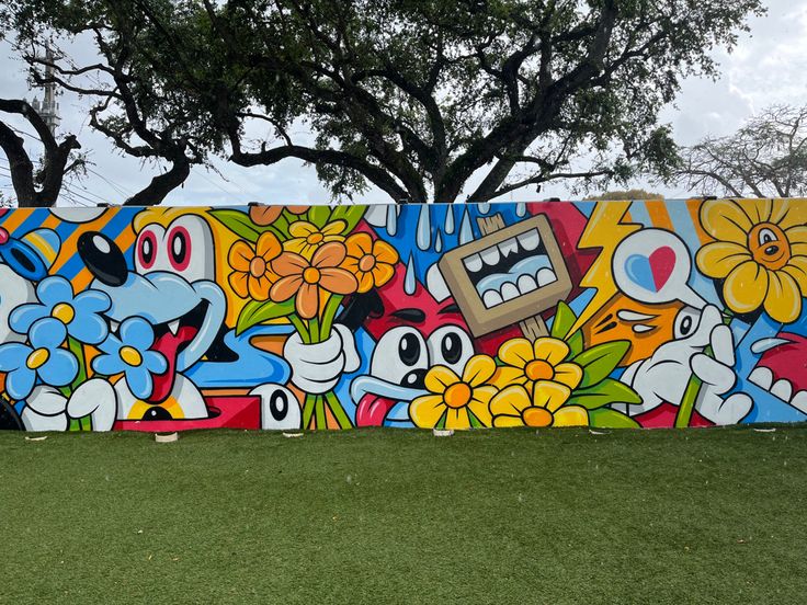 a large colorful mural painted on the side of a building next to a tree and grass area