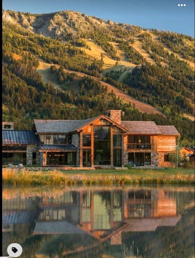 a large house sitting on top of a lush green hillside next to a lake in front of a mountain