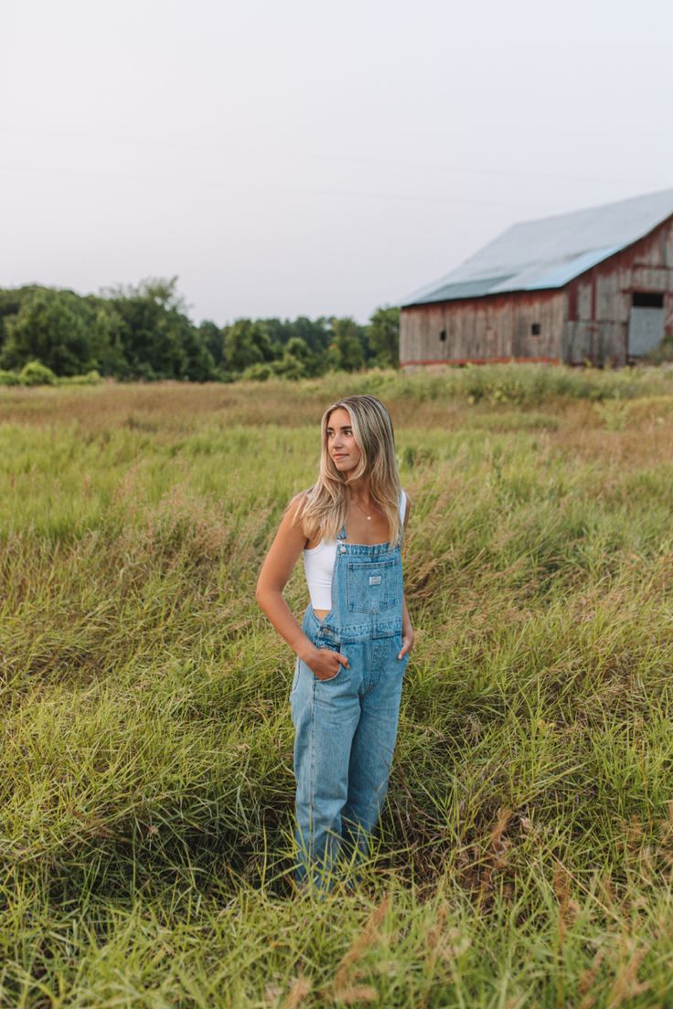 a woman standing in the middle of a field with an old barn in the background