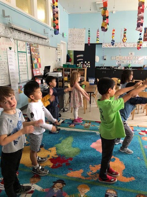 a group of children standing on top of a blue rug in a school room next to each other