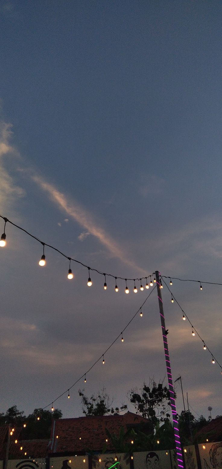 the lights are hanging from the wires in the evening sky above an outdoor venue with tables and chairs