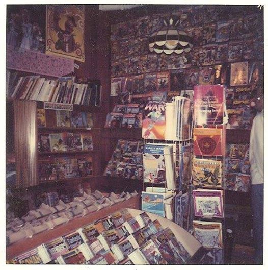 a room filled with lots of books and magazines on shelves next to a man standing in front of a window