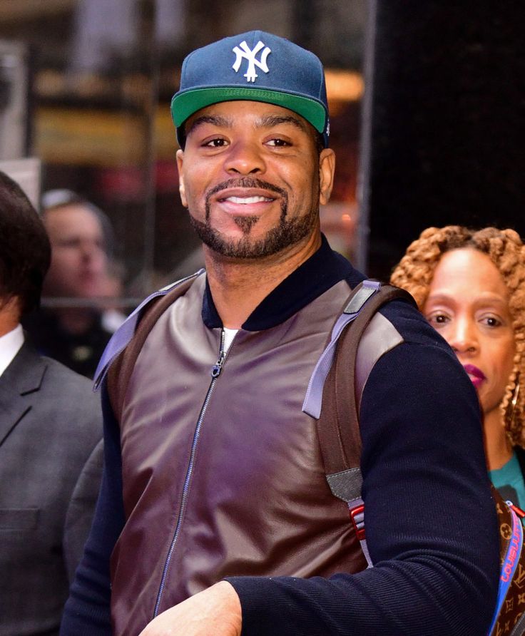 the man is wearing a baseball cap and smiling for the camera as he stands in front of other people