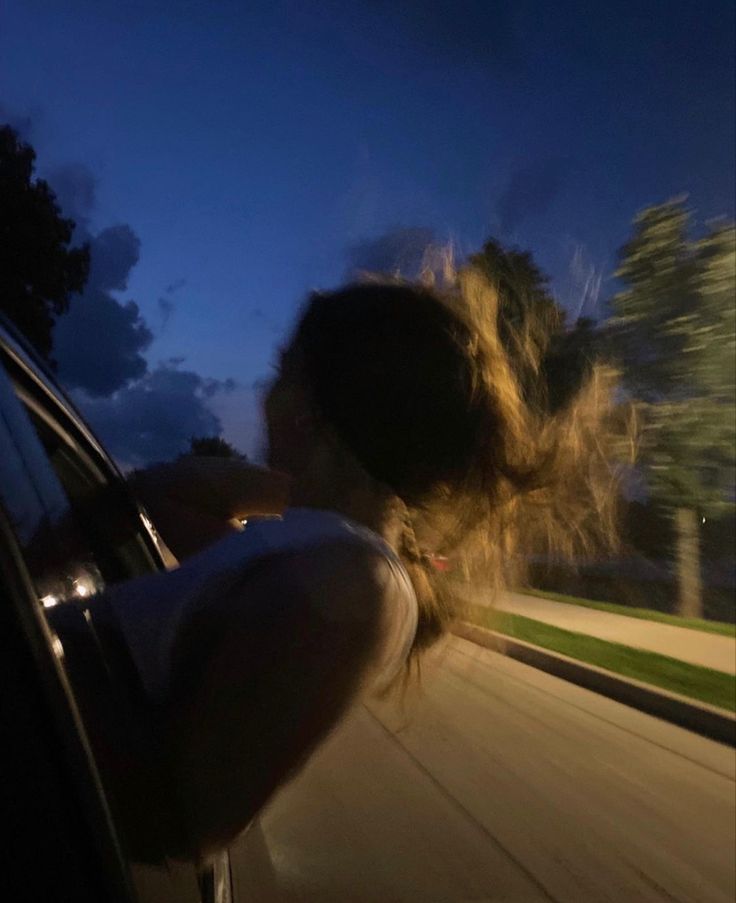 a woman leaning out the window of a car at night with her hair blowing in the wind