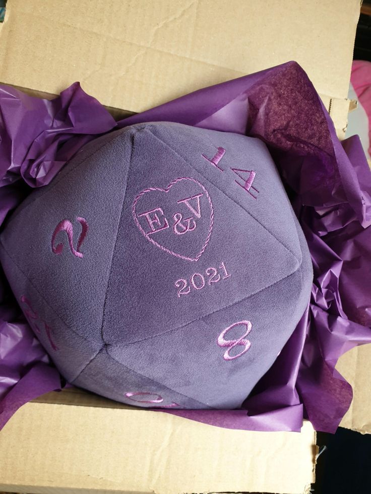 a purple ball with the initials and date on it is in a cardboard box wrapped in purple paper