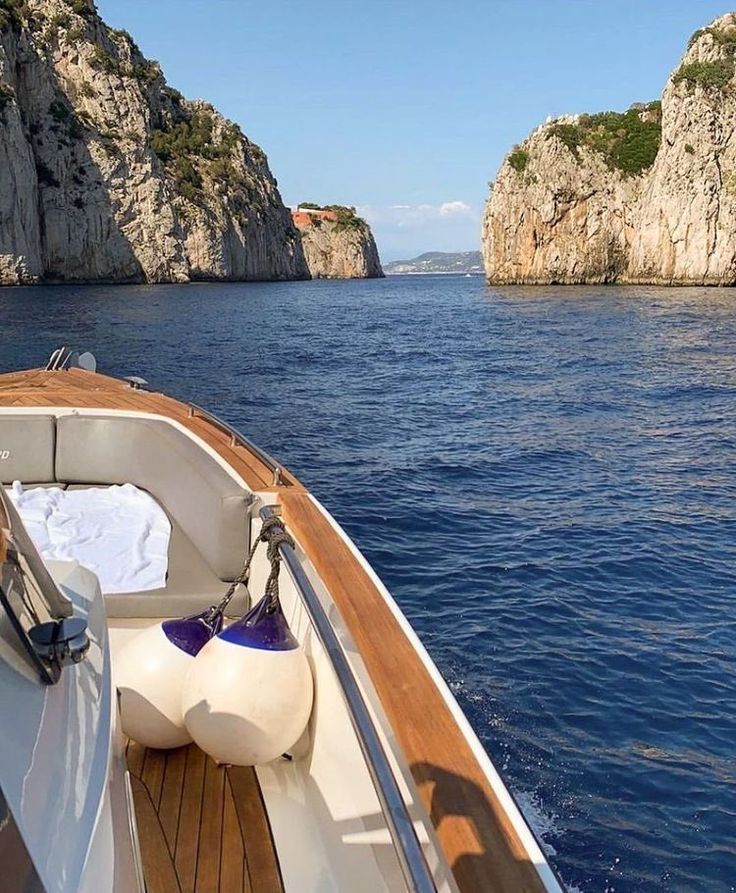 there is a boat that is in the water near some rocks and trees on the shore