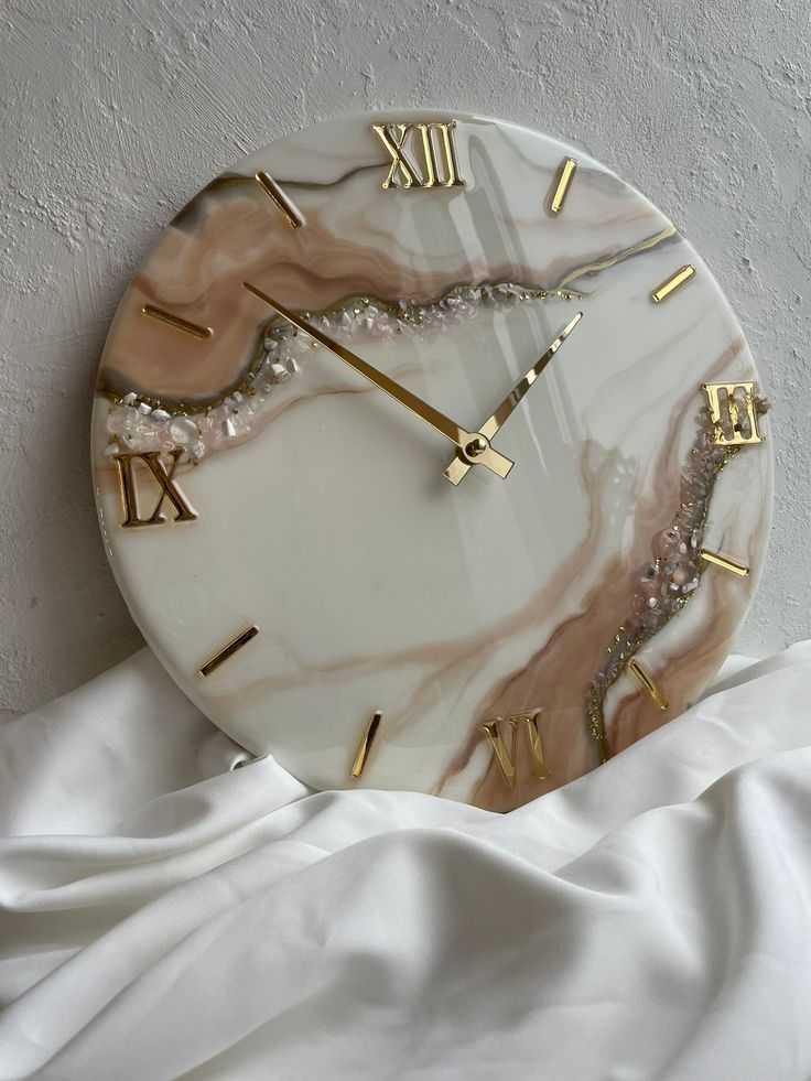 a marble clock with roman numerals and gold hands on a white cloth background