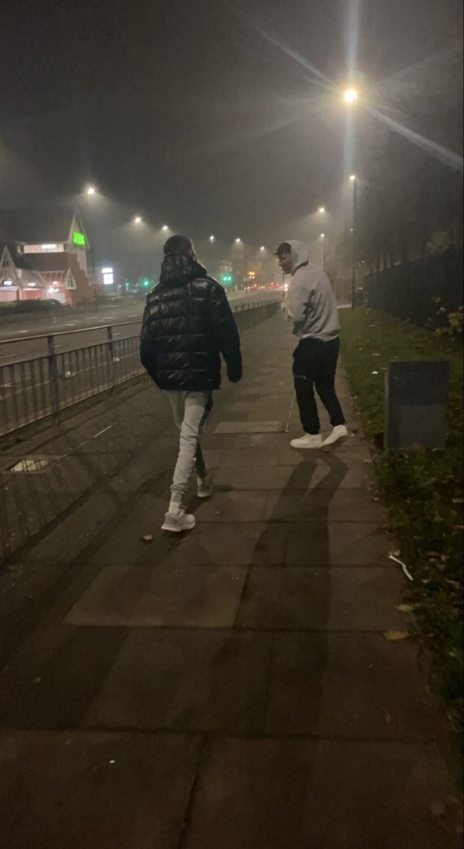 two people walking down a sidewalk at night