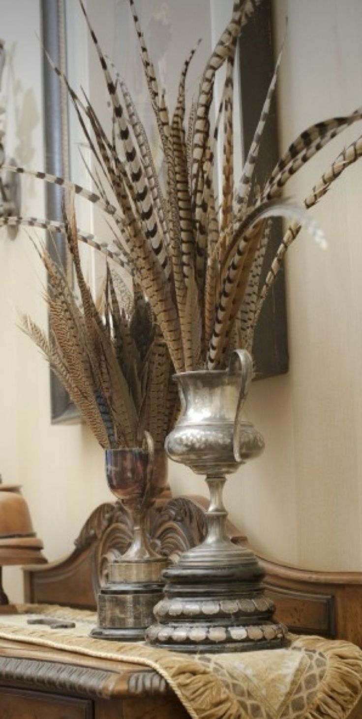 a vase filled with feathers sitting on top of a wooden table next to a mirror