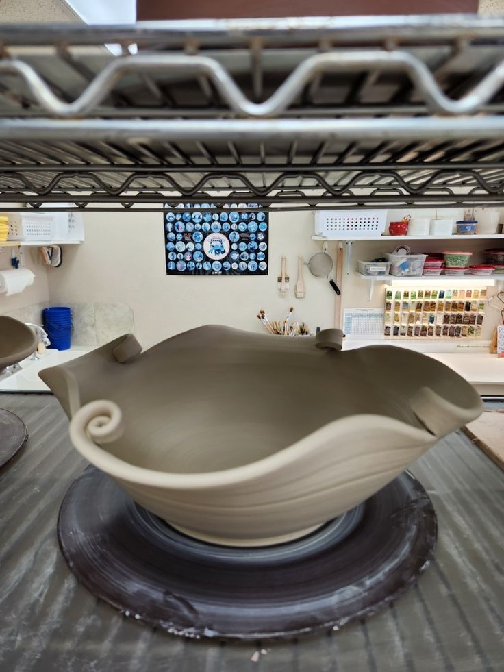 a large bowl sitting on top of a piece of pottery in a room filled with shelves