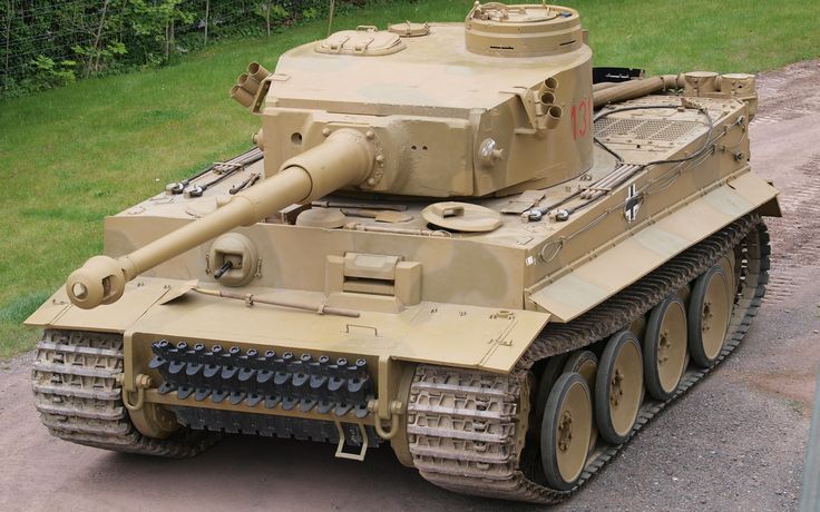 an old tank sitting on the ground in front of a grassy area with trees and bushes behind it