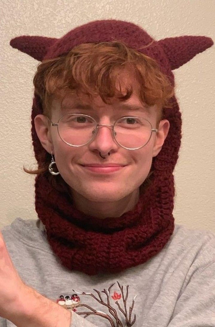 a man wearing a knitted devil hat and scarf with horns on it's head