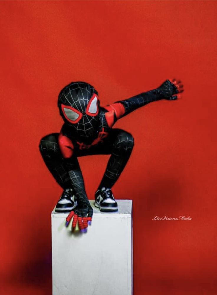 a spider man sitting on top of a white box with his hands in the air