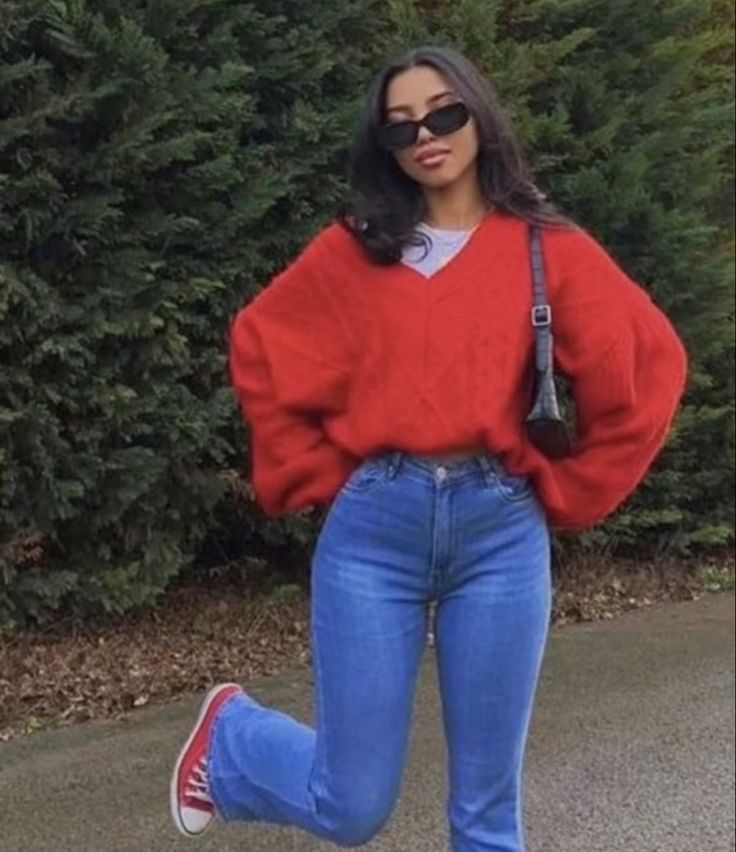 a woman in red sweater and blue jeans is walking down the street with her hands on her hips