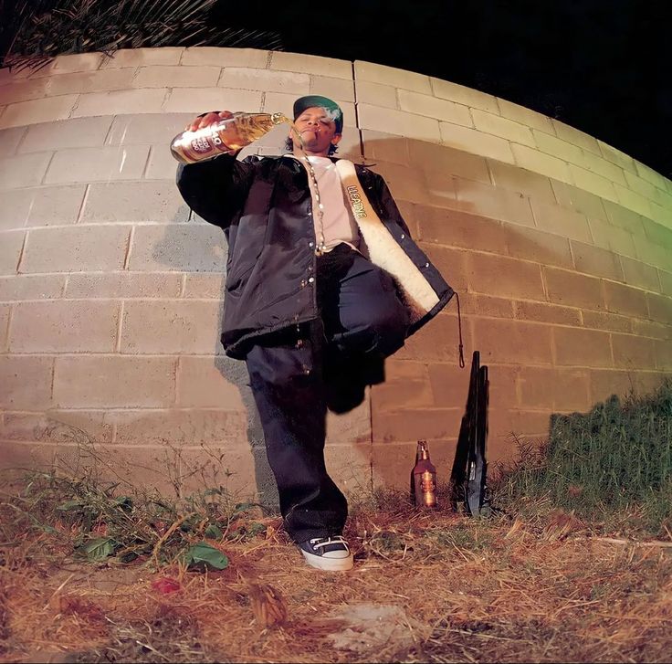 a man standing in front of a brick wall drinking from a bottle