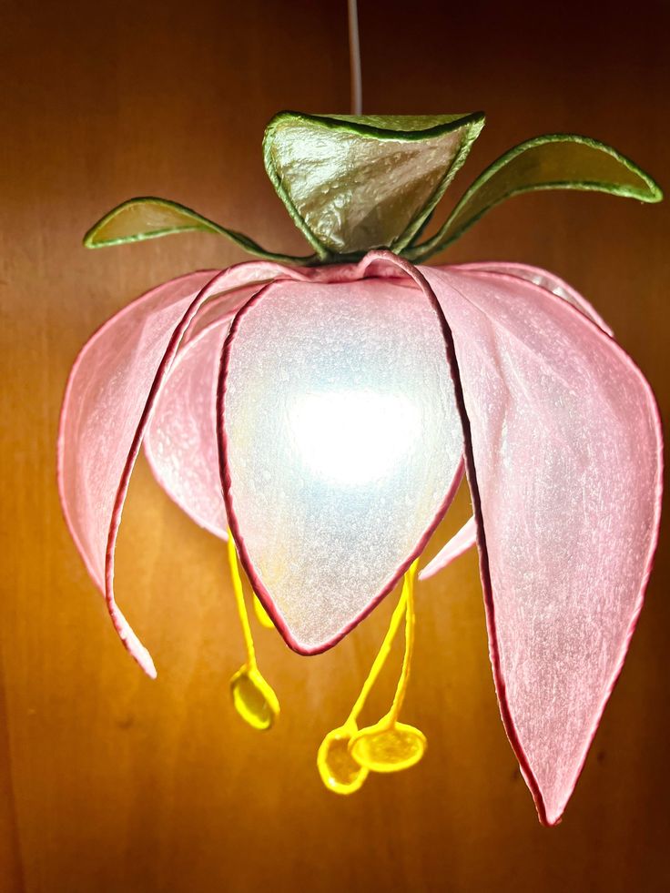 a pink flower hanging from a string on a wooden wall next to a light bulb