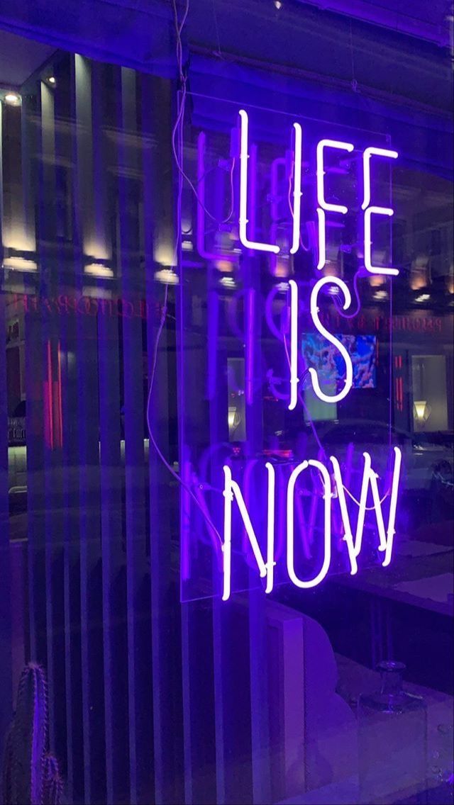 a purple neon sign that says life is now on the glass in front of a window