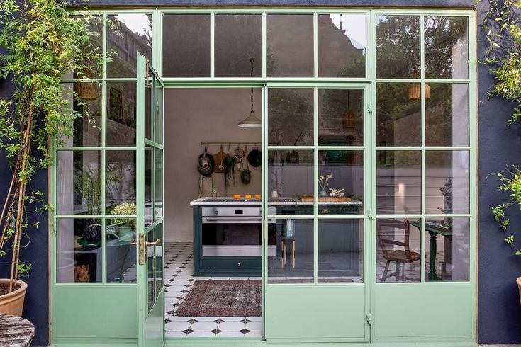 an open kitchen and dining room with green glass doors on the outside, surrounded by potted plants