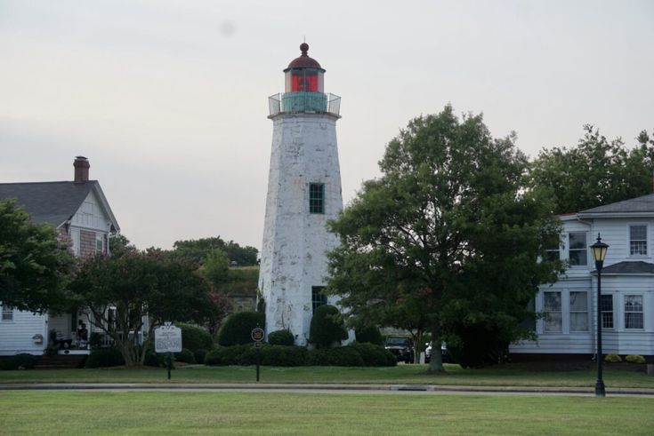 a white and red light house sitting in the middle of a green field next to houses