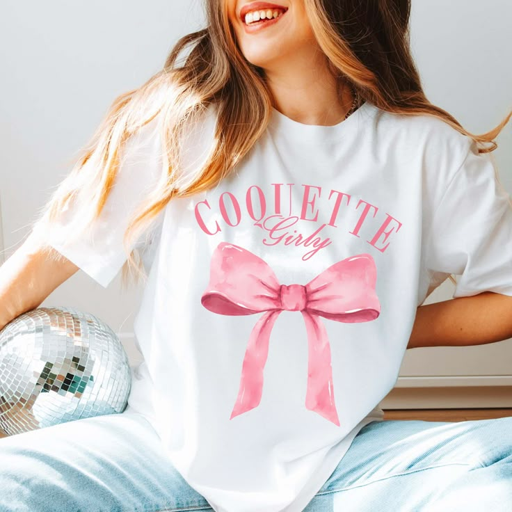 Get girly and flirty with the Coquette Girly Tee! This tee features a big pink bow and a playful "Coquette Girly" text, perfect for adding a touch of fun and femininity to your wardrobe. Stand out from the crowd with this quirky and stylish tee! Design is Printed Direct to Garment. Pink T-shirt With Bow For Summer, Cute Pink T-shirt With Bow Detail, Pink Sorority T-shirt For Summer, Pink Crew Neck T-shirt With Bow, Pink Sorority T-shirt For Spring, Cute Pink Party T-shirt, Cute Spring T-shirt For Gender Reveal, Pink Graphic Tee For Gender Reveal, Cute T-shirt For Spring Gender Reveal