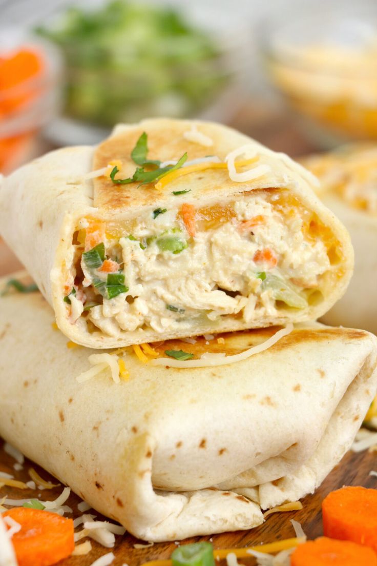 two burritos stacked on top of each other with shredded cheese and vegetables in the background