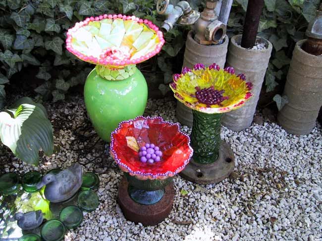 three vases with flowers in them sitting on the ground next to plants and rocks